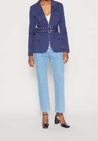 Blazer blu navy con cintura e due tasche frontali, abbinato a jeans dritti azzurri chiari e scarpe con tacco nere. Tessuto dalla texture liscia.