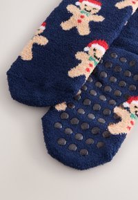 Tmavě modré chlupaté ponožky s perníkovými muži nosícími červené čepice. Podešev má texturované gumové tečky pro lepší přilnavost.