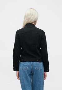 Crna traper jakna sa strukturiranim dizajnom, koja ima ovratnik, vidljive šavove i dugmadi kao ukras u struku.