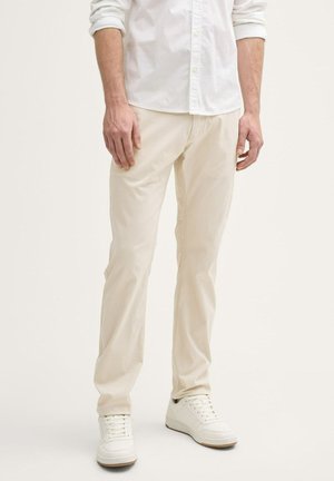 Beige katoenen broeken met een recht model, voorzien van zijzakken en subtiele stiksels, gecombineerd met witte sneakers.