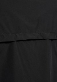 Nahaufnahme eines schwarzen Stoffes mit sichtbarer horizontaler Naht und feinen Falten, die Textur und Nähdetails zeigen.
