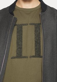 Bavlněná bomber bunda v černé a šedé kostkované úpravě se zapínáním na zip a límcem, kterou nosíte přes olivově zelené tričko s texturovanou temnou grafikou "II."