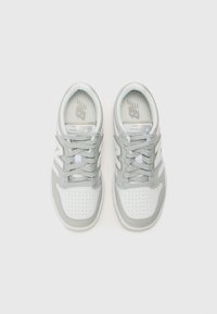 Ljusgrå träningsskor med ovandel i mesh, perforerad tå, snördesign och vita accenter. Har New Balance-logotypen på plåstret.