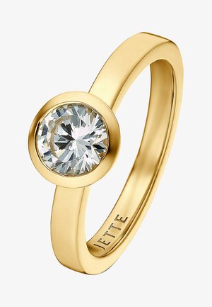 Guldring med en cirkulær, facetteret klar ædelsten sat i en glat bezel. Båndet er slankt med en poleret overflade og graveret med "JETTE."