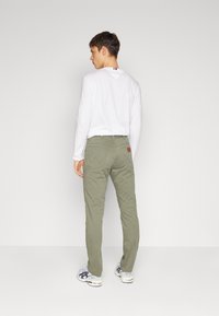 Khawai nadrág, slim fit fazonnal és hátsó zsebekkel, fehér hosszúujjú inggel párosítva. A megjelenést laza sportcipők egészítik ki.