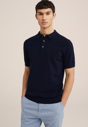Polo de cuello corto color marino, hecho de una tela suave, con un cuello clásico, tapeta de tres botones y corte slim. Combinado con pantalones de color azul claro.