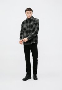 Black and gray plaid flannel shirt with long sleeves and button closure, paired with black slim-fit pants and black lace-up boots.