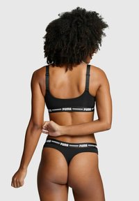 Schwarzes Sport-BH- und String-Set mit verstellbaren Trägern und weißen Puma-Logo-Akzenten. Sanfte Stoffoberfläche, minimalistisches Design.