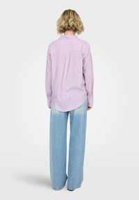 Chemise rose clair à fines rayures verticales, manches longues et ourlet arrondi, associée à un jean bleu clair à jambes larges. Détails de boutons sur les poignets.