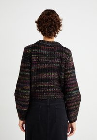 Knitted cardigan in dark tones with colorful, sparkly stripes. Features a relaxed fit, wide sleeves, and a round neckline. Back view shown.
