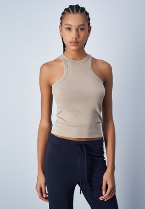 Top corto beige con un cuello alto y diseño de espalda nadadora, hecho de tela elástica; combinado con pantalones jogger azul marino.