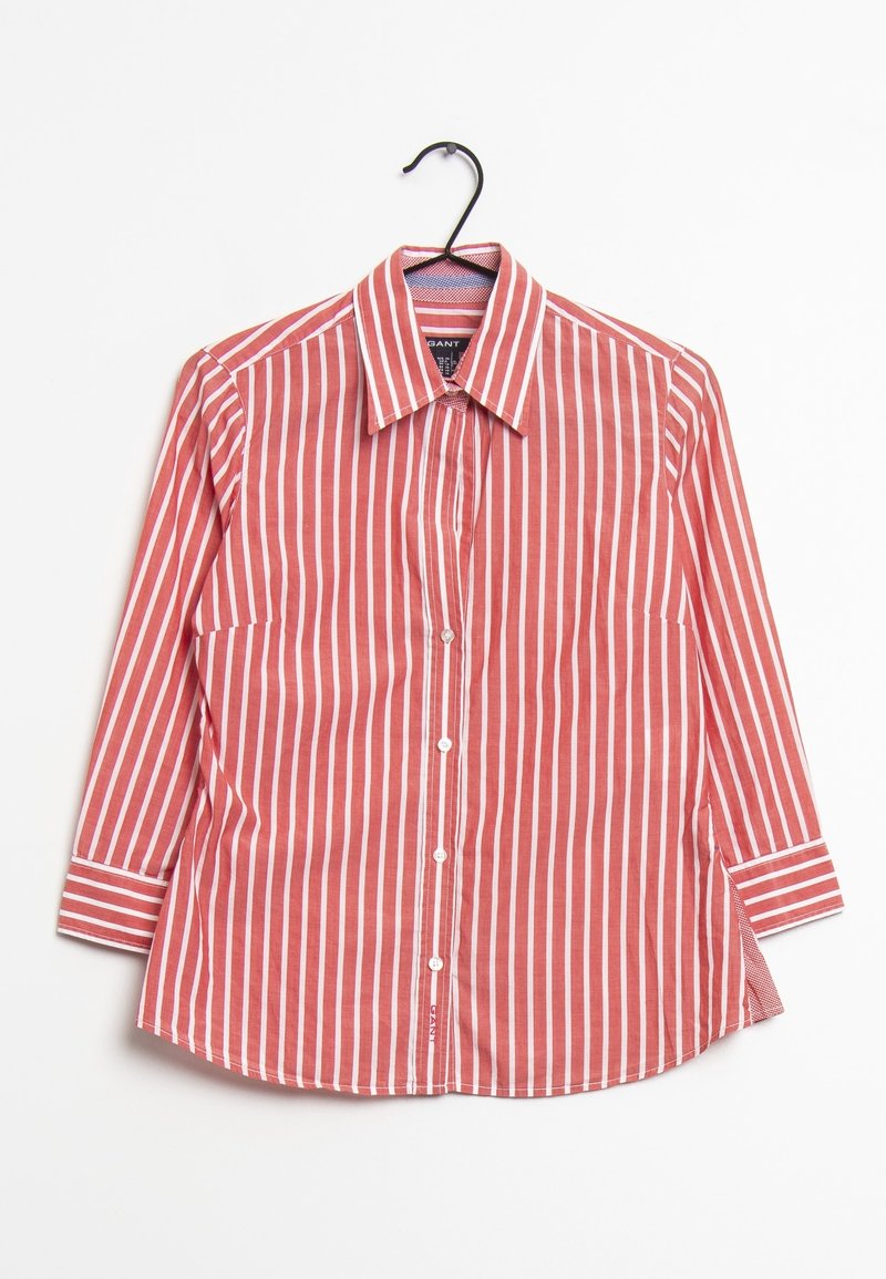 Chemise rayée rouge et blanche à manches longues, avec un col pointu, des boutons sur le devant et des poignets à micro-rayures contrastants. Accrochée à un crochet.
