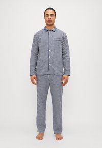 Laivansiniset ja valkoiset ruudulliset pyjama-asusteet, joissa on nappikiinnityksellä varustettu yläosa, kaulus ja rintatasku, yhdessä mukautuvien löysien housujen kanssa.