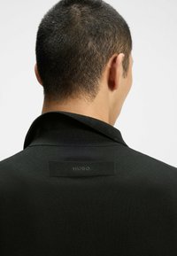 Giacca nera a maglia con un colletto sottile e un'etichetta in tessuto con "HUGO" sul retro. Texture morbida con una vestibilità tailored.
