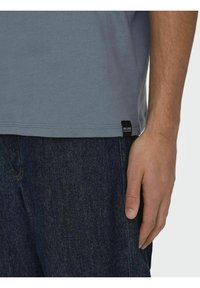 T-shirt grigio in cotone con maniche corte, orlo dritto e un'etichetta nera del marchio cucita in fondo, indossato con jeans di denim scuro.