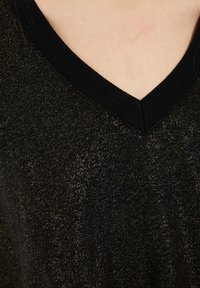 Čierny top s výstrihom do V vyrobený z textúrovanej látky so zlatými odleskami, prepracovaný čierny výstrih a tesné strih.