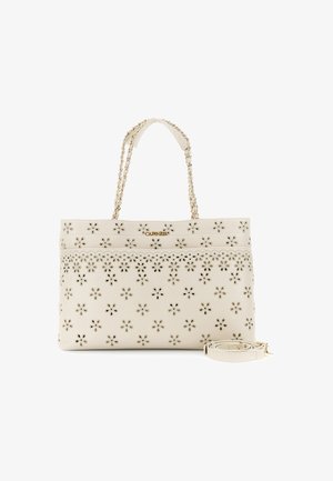 Kremowa torebka z kwiatowym wzorem wycięć, złotymi łańcuszkowymi rączkami oraz odłączanym kremowym paskiem na ramię zwiniętym obok niej.