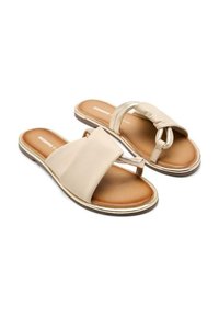 Sandali beige con un'esterno liscio, cinturino ampio e punta rotonda. Presentano un accento attorcigliato e un sottile bordo metallico lungo la suola.