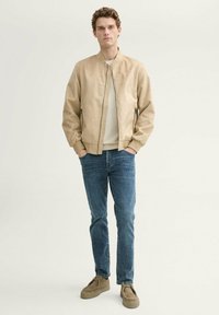 Bež bomber-jakk, mis on valmistatud pehmest materjalist, lukuga ees, soonikkäteosadega, koos helesiniste teksade ja bežede sametist slip-on kingadega.