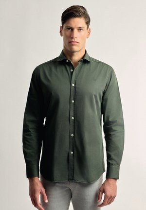 Camisa verde de botonadura con cuello, mangas largas y corte ajustado; cuenta con botones blancos y un logo bordado sutil en el pecho.