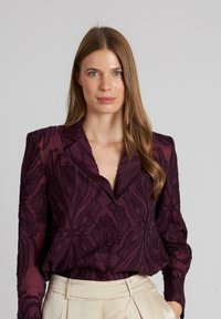 Violet blouse met een gestructureerd bloemenpatroon, op maat gemaakte kraag en knoopsluiting. Lange mouwen en lichtjes getailleerd in de taille.