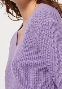 Suéter de punto morado con un diseño de escote en V. La textura es acanalada y la tela parece suave y acogedora.