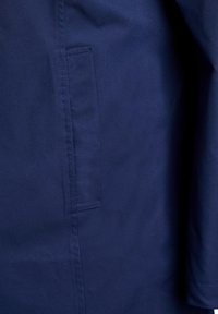 Granatowy płaszcz o gładkiej fakturze, z boczną kieszenią i schludnymi szwami. Projekt jest prosty, bez widocznych metalowych elementów.