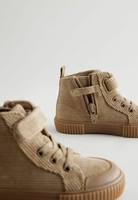 Bottes chelsea en velours côtelé beige avec une surface texturée, des semelles en caoutchouc, des fermetures à lacets et à zip, et une languette de talon pour un enfilage facile.