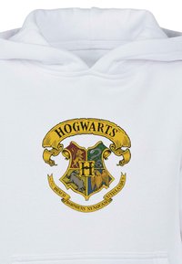 Witte hoodie met het Hogwarts-wapen in levendige kleuren en ingewikkelde details, met vier huis-symboolen en een lint.