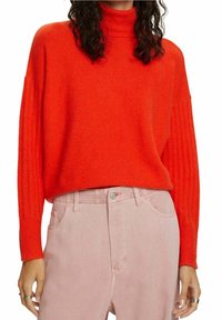 Roter Rollkragenpullover mit gerippten Ärmeln, aus weichem Material, kombiniert mit hellrosa, hoch taillierten Jeans.