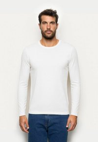 Langärmliges weißes T-Shirt aus weichem Stoff mit Rundhalsausschnitt und figurbetontem Schnitt, kombiniert mit dunkelblauen Jeans.