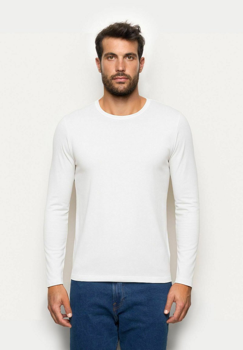 Langärmliges weißes T-Shirt aus weichem Stoff mit Rundhalsausschnitt und figurbetontem Schnitt, kombiniert mit dunkelblauen Jeans.