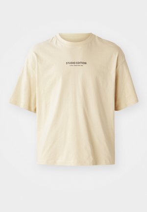 Beige puuvillane t-särk ümarate nööbiga, lühikeste varrukatega ning rinnal must print tekstiga "STUDIO EDITION".