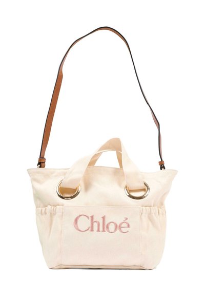 Beżowa torba typu tote wykonana z płótna z różowym logo „Chloé”, dwoma krótkimi uchwytami przechodzącymi przez metalowe pierścienie oraz długim regulowanym brązowym paskiem na ramię.