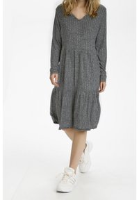 Grijze jurk met lange mouwen en V-hals, van textuur ribbelstof, gelaagd ontwerp en een knie-lange zoom, gecombineerd met witte sport sneakers.