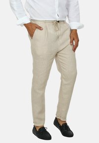 Pantaloni in lino beige con vita a cordoncino e tasche laterali, caratterizzati da una vestibilità comoda e orli alla caviglia. Abbinati a scarpe da barca nere.