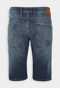 Pantalones cortos de mezclilla en azul oscuro con un acabado desgastado, que presentan dos bolsillos traseros con detalles de costura y un parche de cuero marrón en la cinturilla.