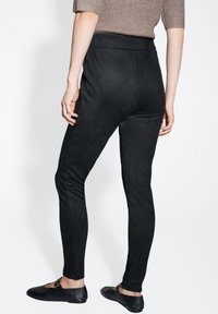 Leggings neri aderenti con una texture liscia simile al suede. Vita alta e gambe affusolate. Indossati con scarpe nere flat.