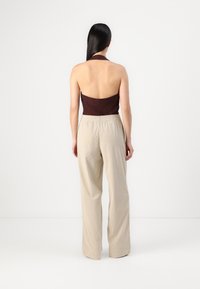 Top a halter marrone con schiena scoperta, abbinato a pantaloni larghi plissettati beige chiaro. Tessuto liscio, design semplice, colori neutri.
