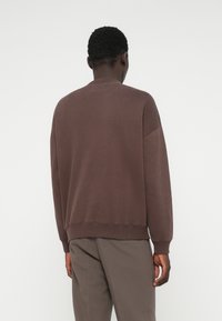 Καφέ sweatshirt με στρογγυλή λαιμόκοψη, ριχτές μανσέτες και στρίφωμα. Λείο υλικό με άνετη εφαρμογή. Συνδυάζεται με γκρι κομμένα παντελόνια.