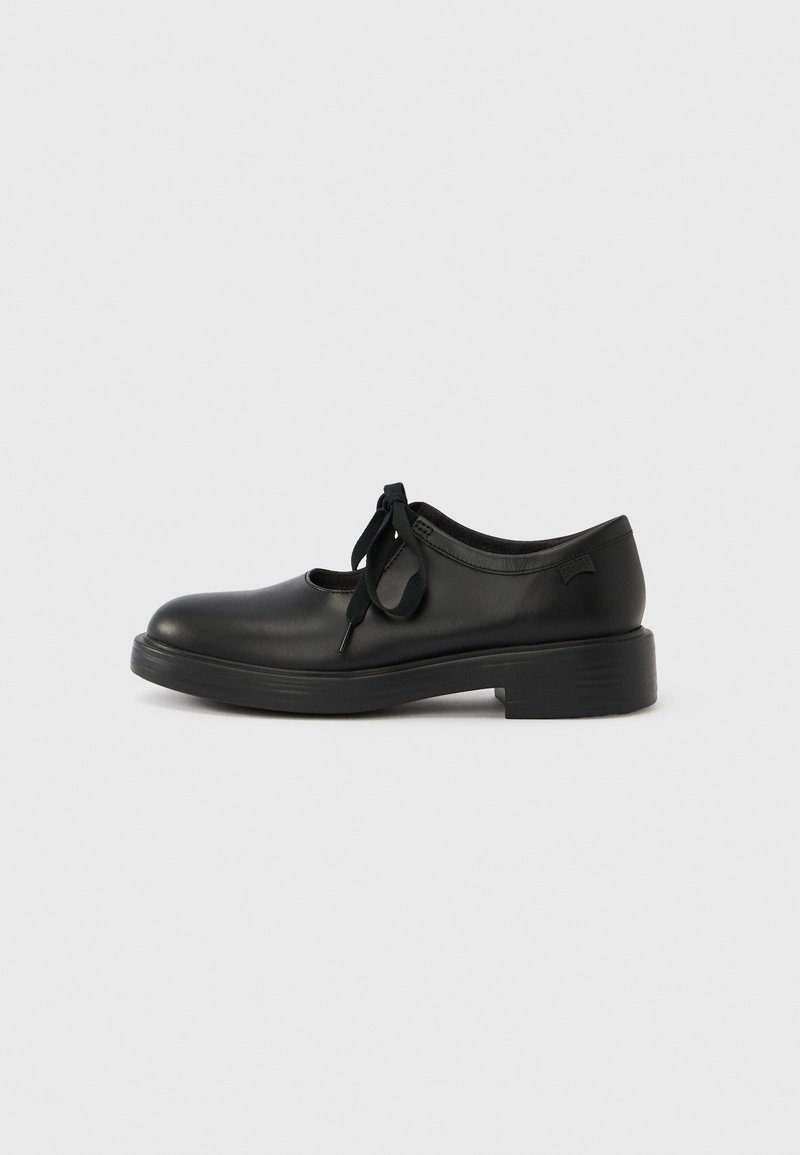 Chaussure en cuir noir avec un bout arrondi, une découpe à l'avant et un lacet décoratif. Talon épais et finition mate. Texture lisse et détails minimalistes.