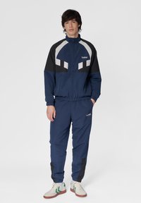 Marintröja med vita och svarta accenter. Jackan har hög krage och dragkedja. Byxorna har elastiska mudd och logodetalj.