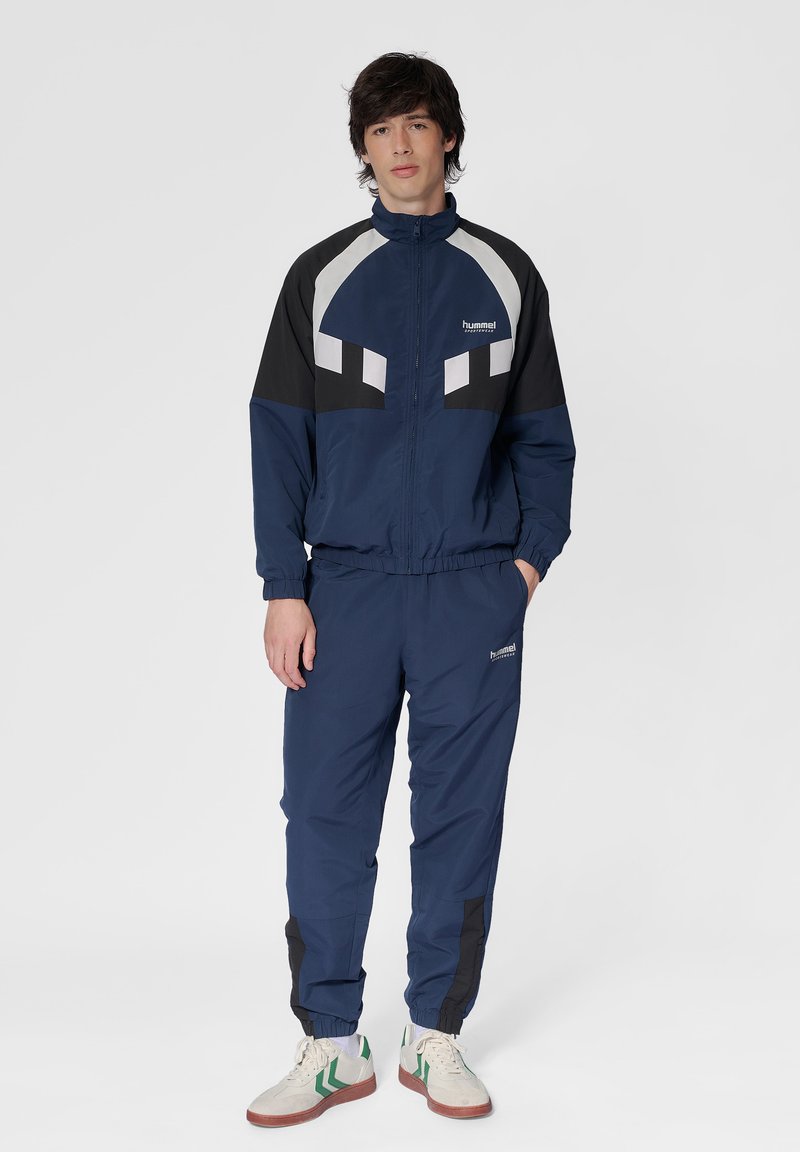 Marintröja med vita och svarta accenter. Jackan har hög krage och dragkedja. Byxorna har elastiska mudd och logodetalj.