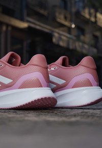 Paire de chaussures de sport roses avec semelles blanches placées sur une surface en pierre dans un environnement urbain extérieur.