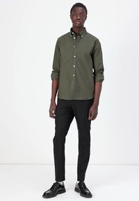 Cămașă verde închis cu mâneci lungi, asortată cu pantaloni negri și pantofi negri lucioși. Design simplu, fără modele sau accente vizibile.