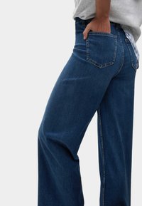 Jeans in denim blu a vita alta e gamba larga presentano un classico design a cinque tasche e leggeri segni di sbiadimento, con una texture leggera.