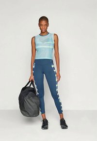 Heledad helesinine topp, sobiv tumedasinised retuusid kollaste ja valgete külgribadega, must spordikott, sportlikud jalanõud, sile kangas.