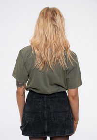 Olive green oversized t-shirt, short sleeves, back view; paired with a black denim mini skirt featuring two back pockets.