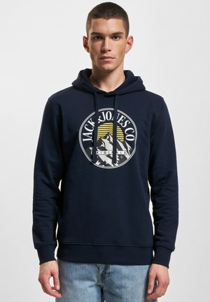 Navy blue hoodie made of cotton, featuring a front white graphic logo with mountains and sun. It has a drawstring hood and ribbed cuffs.