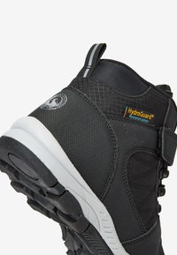 Schwarzer wasserdichter Stiefel mit einem Obermaterial aus strukturiertem Stoff, HydroGuard®-Markierung und einer weißen Gummisohle. Verfügt über verstellbare Riemen für eine optimale Passform.